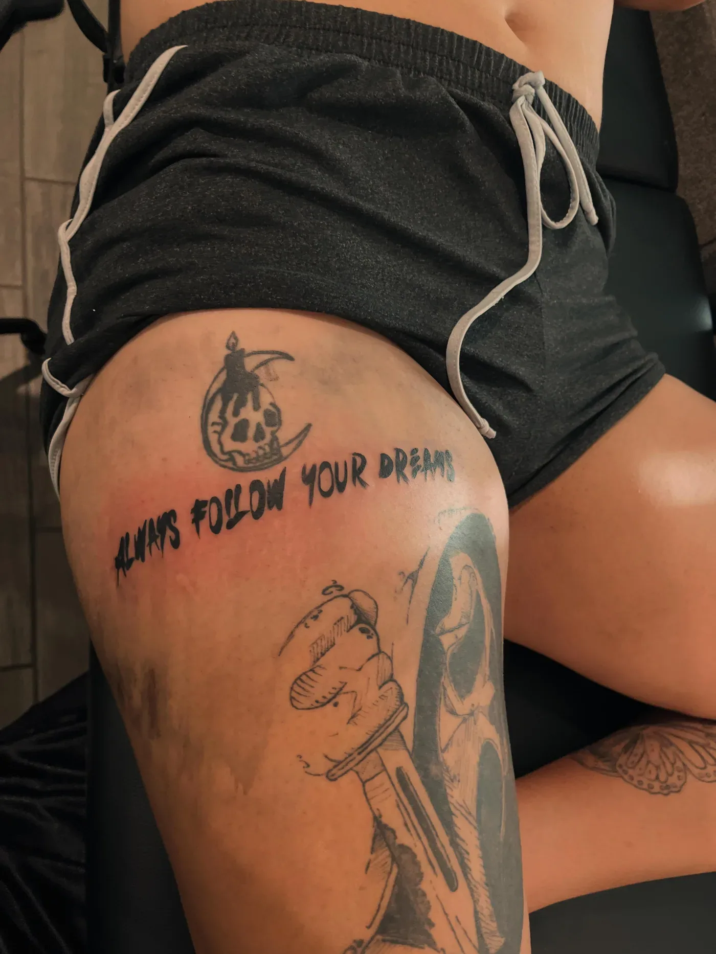 Thigh tattoo with script lettering and a figure in black and gray