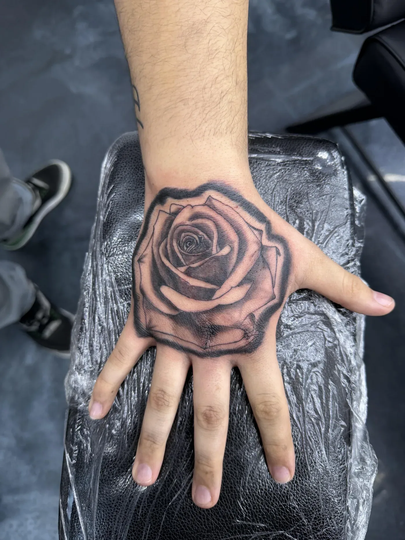 Black and gray rose tattooed across the back of a client's hand