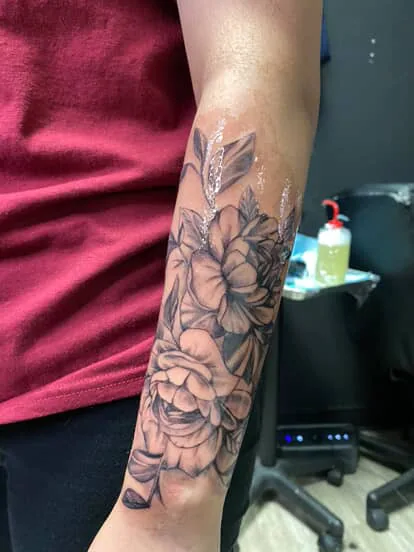 Floral black and gray tattoo running up a client's forearm