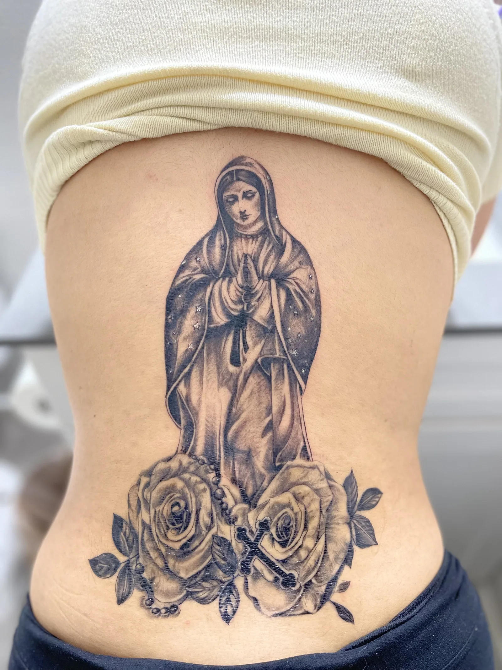 Large black and gray religious tattoo across a client's hip and back
